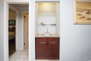 Indoor wet bar featuring light tile patterned floors, light countertops, open shelves, and dark brown cabinetry
