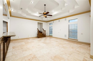 Tiled empty room with a raised ceiling, ceiling fan, and crown molding