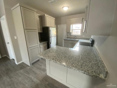 Kitchen featuring stove, freestanding refrigerator, a peninsula, light stone counters, and dark wood finished floors