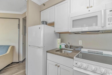Kitchen with white appliances, ornamental molding, white cabinets, light wood-style floors, and dark stone countertops
