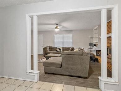 Living room with a textured ceiling, a fireplace, a ceiling fan, and light tile patterned flooring