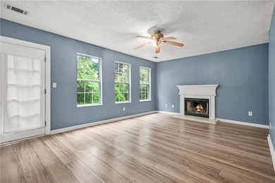 Unfurnished living room with a ceiling fan, a textured ceiling, wood finished floors, and a lit fireplace