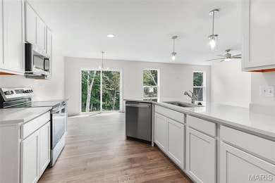 Kitchen with stainless steel appliances, white cabinets, hanging light fixtures, light wood-style flooring, and recessed lighting