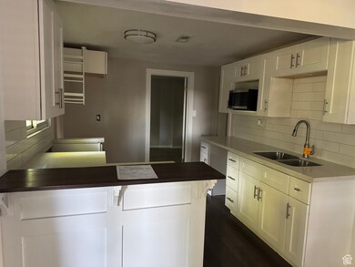 Kitchen featuring tasteful backsplash, a peninsula, white cabinets, and dark wood-style flooring