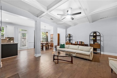 Living area with coffered ceiling, a ceiling fan, beamed ceiling, dark wood-style flooring, and baseboards