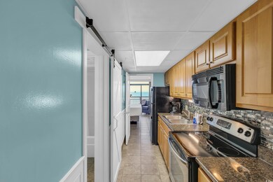 Kitchen with stainless steel range with electric cooktop, black microwave, a barn door, decorative tile backsplash, and dark countertops