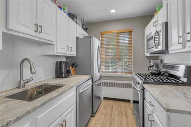 Kitchen with decorative backsplash, stainless steel appliances, white cabinets, radiator heating unit, and light wood finished floors