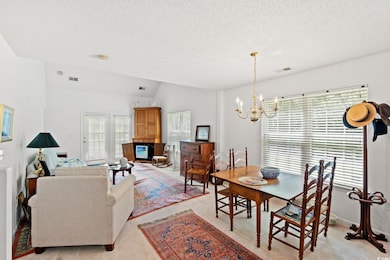 Dining room featuring lofted ceiling, a chandelier, light colored carpet, and a textured ceiling
