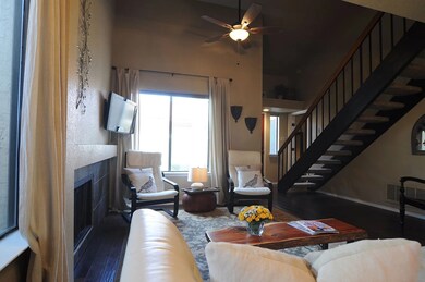 Living room with dark wood-style flooring, stairs, a tiled fireplace, a ceiling fan, and a high ceiling