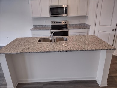 Kitchen with stainless steel appliances, light stone counters, and white cabinets