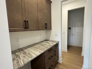 Bar area featuring dark brown cabinets, light stone countertops, and light wood-style flooring