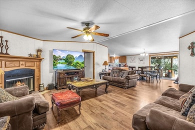 Living area with wood finished floors, ornamental molding, a glass covered fireplace, lofted ceiling, and ceiling fan