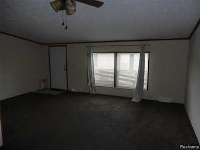 Empty room featuring crown molding, dark carpet, ceiling fan, and a textured ceiling