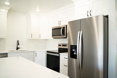 Kitchen with stainless steel appliances, white cabinetry, recessed lighting, and light stone counters