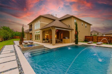 Take a look at this stunning view of the backyard featuring the pool with water feature and spa, lush landscaping and the covered back patio with outdoor kitchen.