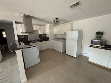Kitchen with white cabinets, freestanding refrigerator, light tile patterned floors, a peninsula, and a textured ceiling