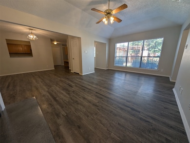 Unfurnished living room featuring a textured ceiling, dark wood finished floors, a ceiling fan, vaulted ceiling, and a chandelier
