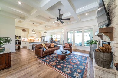 Living room with ceiling fan with notable chandelier, a fireplace, light hardwood / wood-style flooring, and coffered ceiling