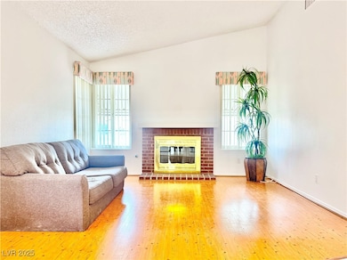 Living room with vaulted ceiling, hardwood / wood-style flooring, a brick fireplace, and a textured ceiling