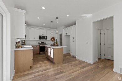 Kitchen with white cabinets, hanging light fixtures, appliances with stainless steel finishes, recessed lighting, and a kitchen island.