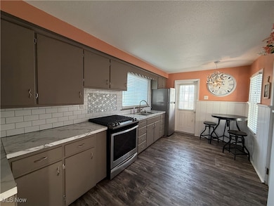 Kitchen featuring stainless steel appliances, dark wood finished floors, light countertops, and decorative light fixtures