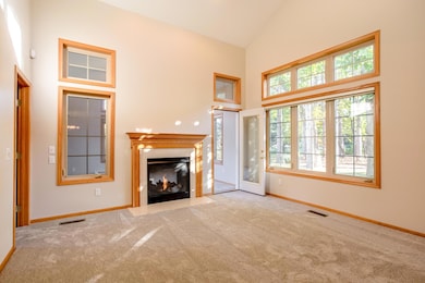 Bright and spacious living room featuring vaulted ceilings, a cozy 2-sided gas fireplace, and large windows that fill the space with natural light.