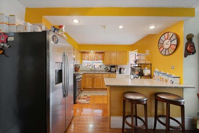 Kitchen featuring stainless steel appliances, a kitchen bar, a peninsula, light wood-style floors, and light stone countertops