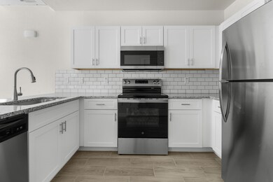 Kitchen featuring stainless steel appliances, white cabinetry, light stone countertops, and backsplash
