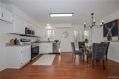 Kitchen featuring stainless steel appliances, hardwood / wood-style floors, white cabinetry, an inviting chandelier, and a healthy amount of sunlight