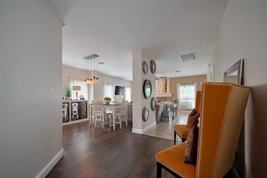 Open-concept living and dining area with warm hardwood floors, modern lighting, and ample natural light from large windows.