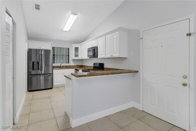 Kitchen featuring dark stone counters, white cabinets, stainless steel refrigerator with ice dispenser, kitchen peninsula, and black range