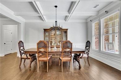 Dining area with a chandelier, beam ceiling, coffered ceiling, wood finished floors, and a wainscoted wall