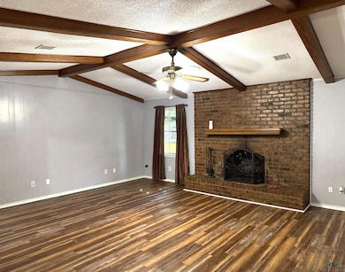 Unfurnished living room featuring wood finished floors, a brick fireplace, a ceiling fan, a textured ceiling, and wood walls