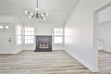 Unfurnished living room with light wood-style floors, a brick fireplace, a textured ceiling, a chandelier, and vaulted ceiling