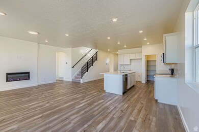 Kitchen featuring open floor plan, a kitchen island with sink, a glass covered fireplace, light wood-style flooring, and white cabinets