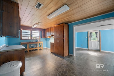 Kitchen featuring wooden ceiling, healthy amount of natural light, brown cabinetry, light countertops, and dark stone finish flooring