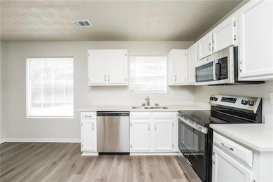 Kitchen with stainless steel appliances, light wood-style floors, white cabinets, and healthy amount of natural light