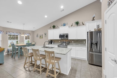 Kitchen with vaulted ceiling, stainless steel appliances, decorative light fixtures, decorative backsplash, and light tile patterned floors