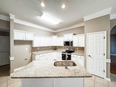 Kitchen with stainless steel appliances, crown molding, white cabinets, light tile patterned flooring, and a sink