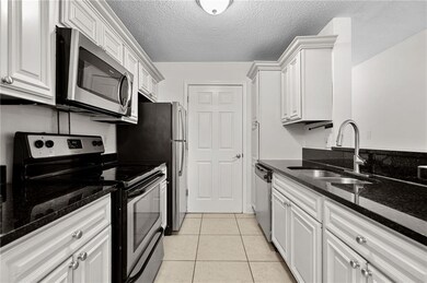 Kitchen with appliances with stainless steel finishes, white cabinets, light tile patterned floors, dark stone counters, and a textured ceiling