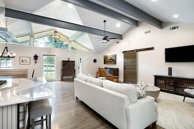 Living room with hardwood / wood-style flooring, ceiling fan with notable chandelier, high vaulted ceiling, beamed ceiling, and a barn door