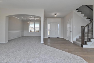 Carpeted foyer entrance featuring stairs, wainscoting, wood finished floors, a notable chandelier, and coffered ceiling