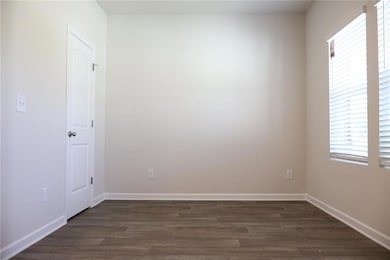 Spare room with dark wood-type flooring and baseboards
