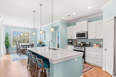 Kitchen featuring ornamental molding, stainless steel appliances, tasteful backsplash, white cabinetry, and light wood-style floors