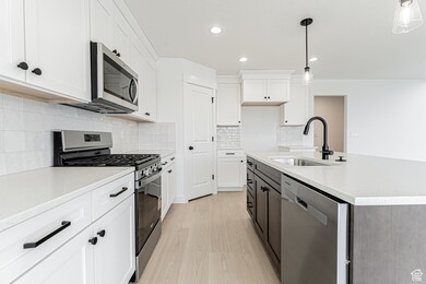 Kitchen featuring stainless steel appliances, white cabinets, light stone counters, light wood-style floors, and recessed lighting
