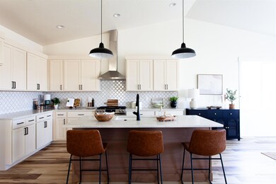 Kitchen with wall chimney range hood, vaulted ceiling, stainless steel range with gas cooktop, a kitchen breakfast bar, and light wood-style flooring
