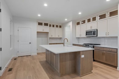 Kitchen featuring tasteful backsplash, glass insert cabinets, white cabinets, light wood-style flooring, and recessed lighting