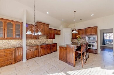Kitchen featuring a center island with sink, hanging light fixtures, stainless steel appliances, stone countertops, and decorative backsplash