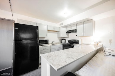 Kitchen featuring black appliances, a peninsula, a breakfast bar, and under cabinet range hood