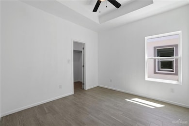 Unfurnished room with a raised ceiling, baseboards, wood finished floors, and ceiling fan